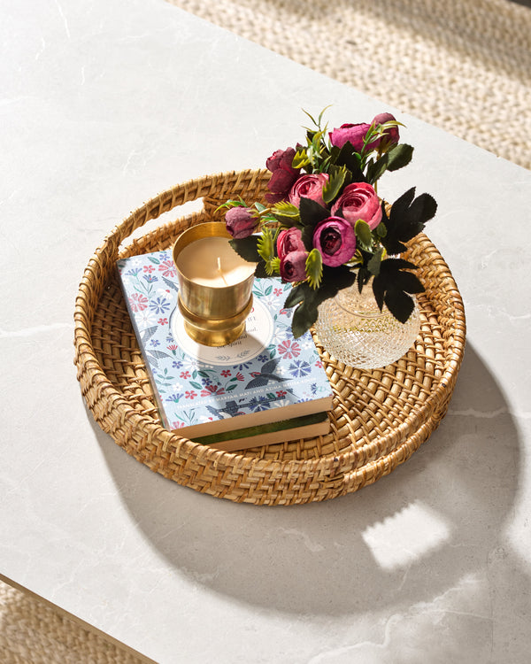 Golden candle in glass holder with pink roses on round rattan tray
