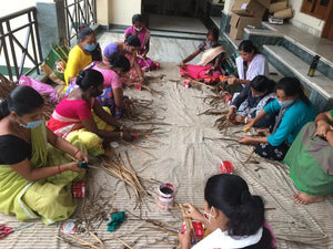 Artisans in colorful saris weave natural fiber crafts on striped mat