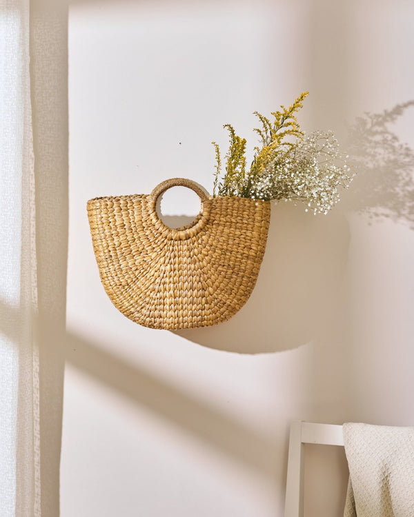 Water hyacinth semi-circular handbag with woven straw basket holding dried yellow and white flowers
